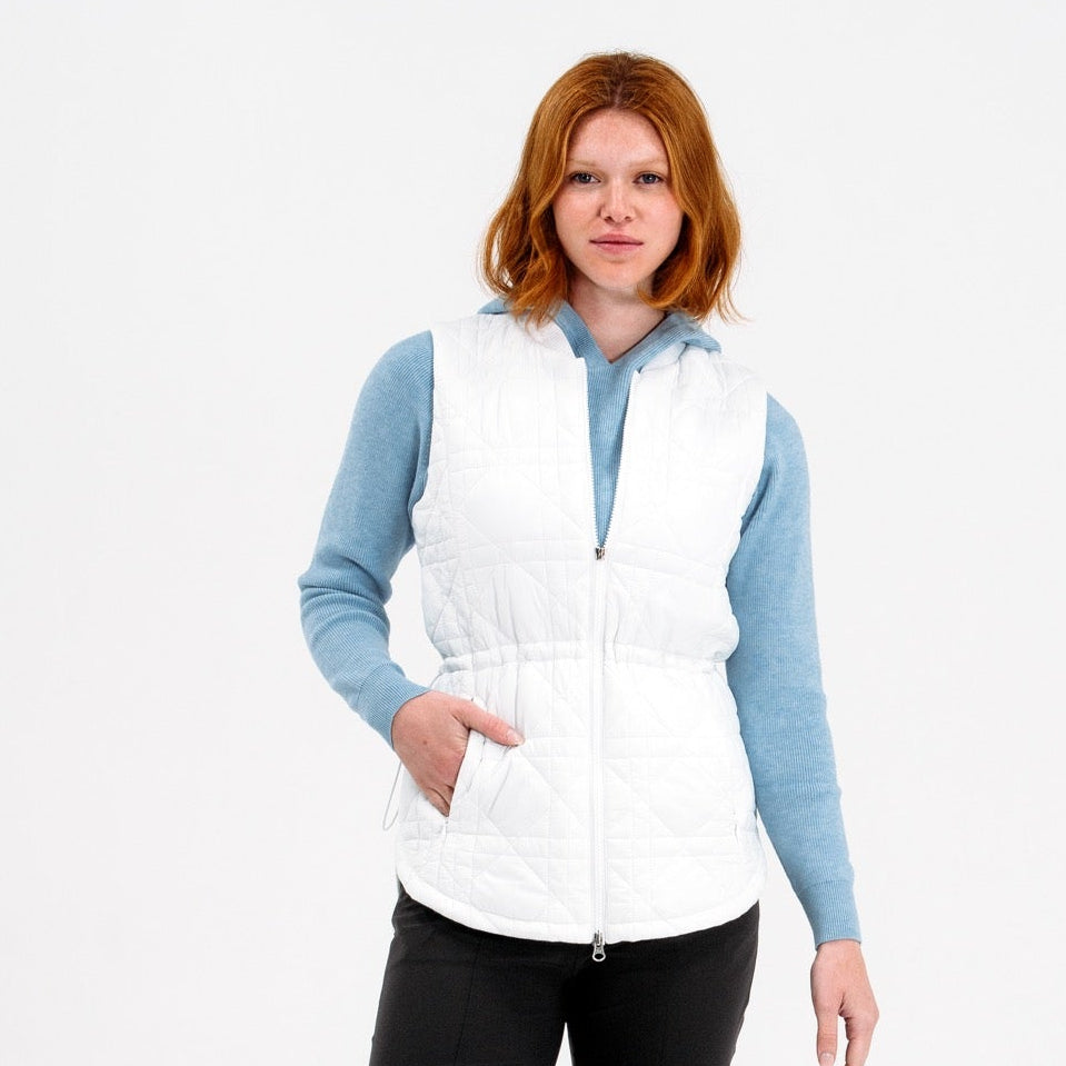 Woman wearing a white puffer vest over a blue long-sleeve shirt on a white background
