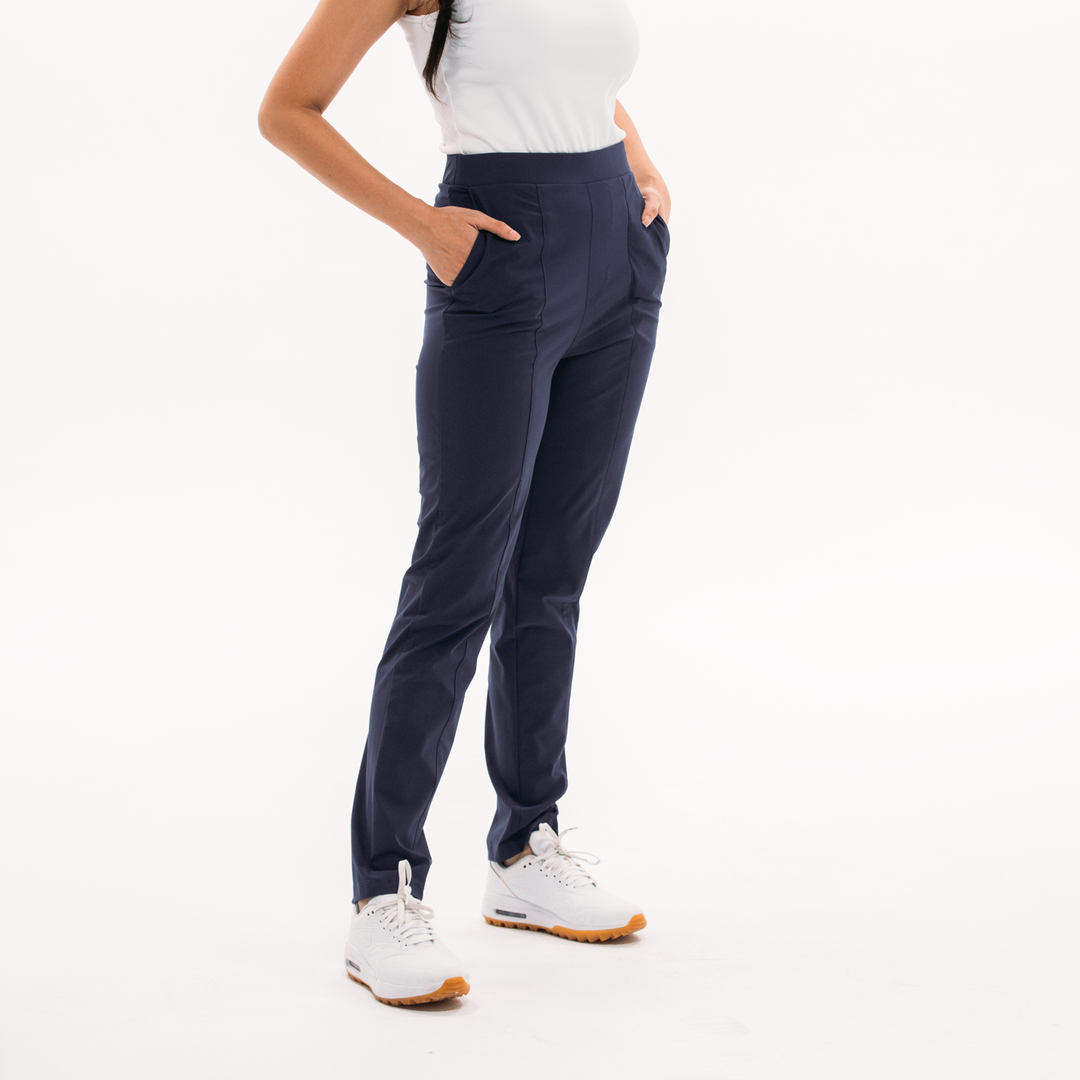 Woman wearing a white sleeveless top and dark blue pants on a white background