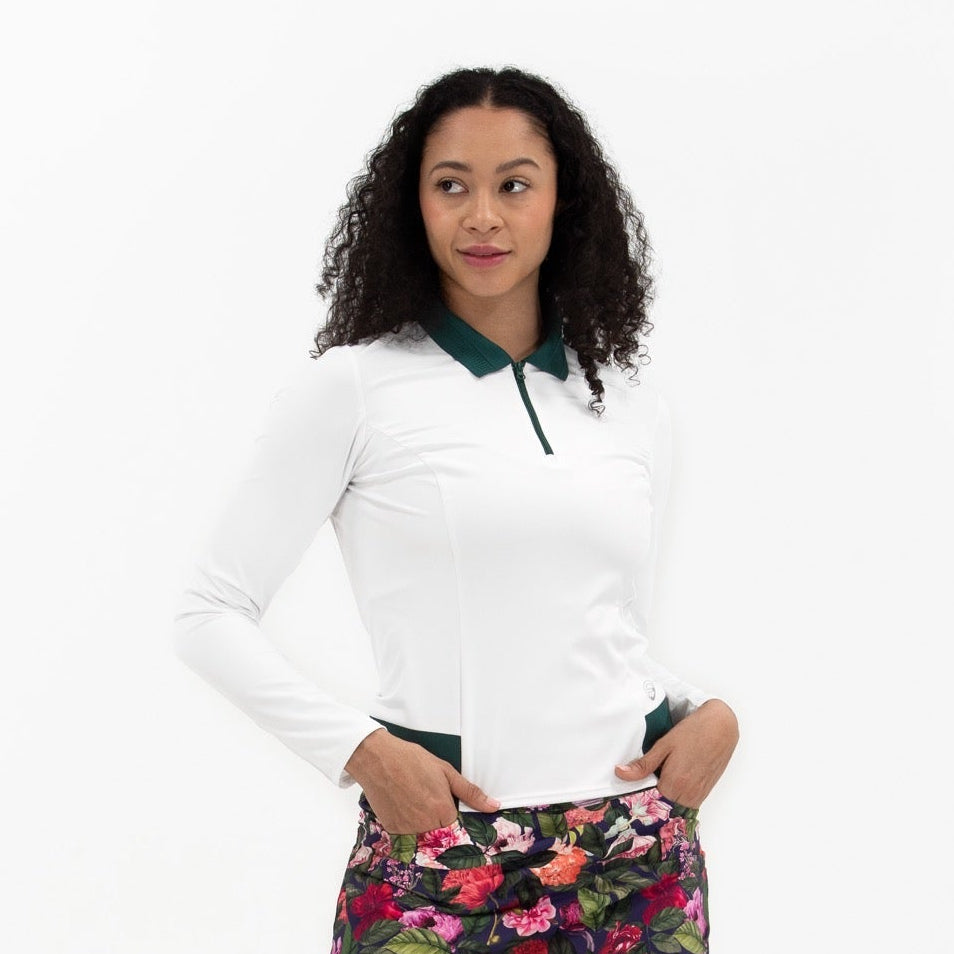 A woman modeling a white long-sleeve polo shirt and a dark floral mini skirt with pink, red, and green flowers, paired with white sneakers and dark socks, against a plain white background.