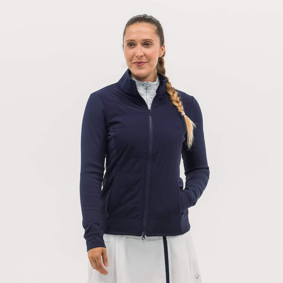 Woman wearing a navy jacket and white skirt on a light gray background