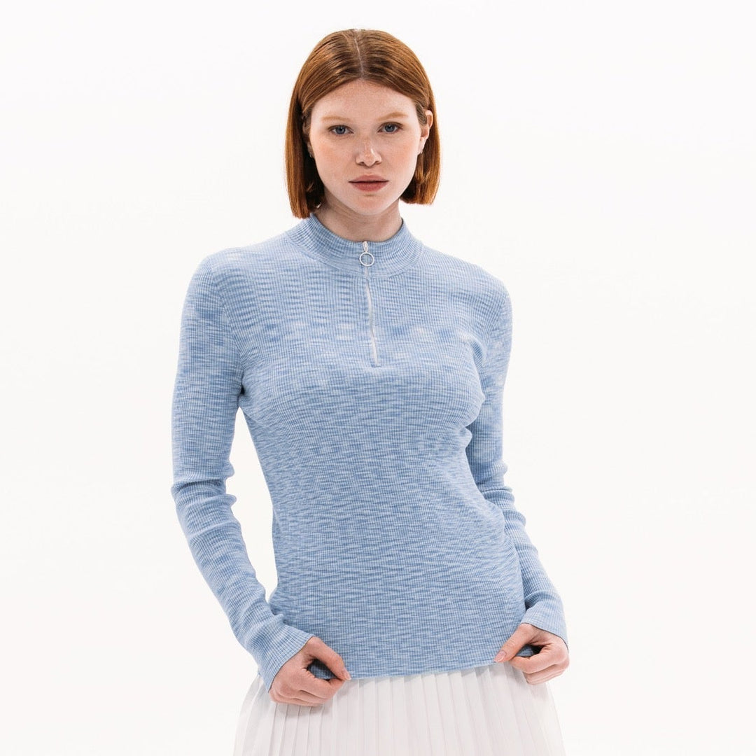 Woman wearing a blue long-sleeve top and white skirt on a white background