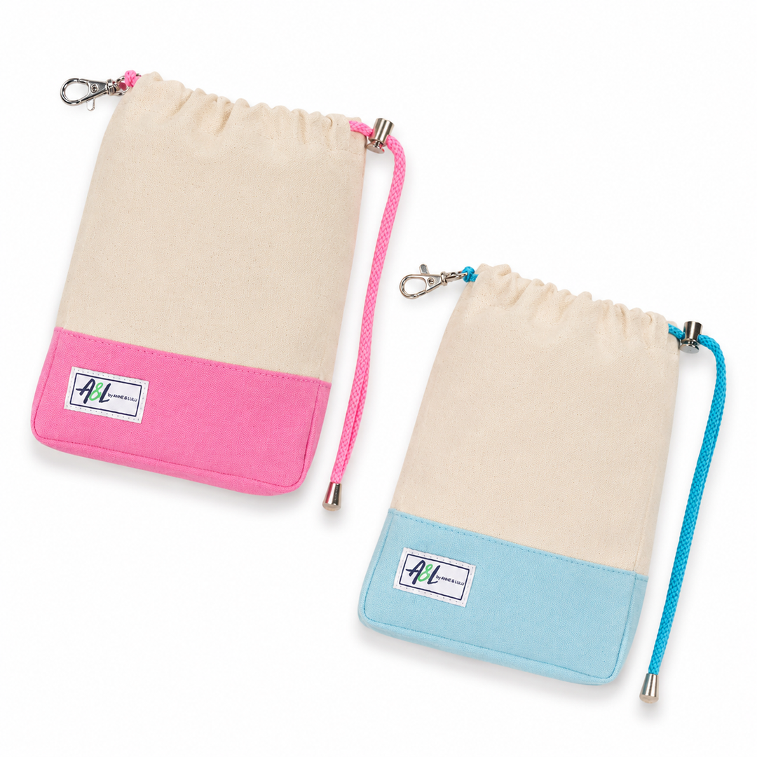 Two fabric drawstring pouches on a white background, one in pink and one in light blue. Both have a cream upper section, a contrasting bottom panel in pink and blue respectively, a white brand patch, and a metal clip.