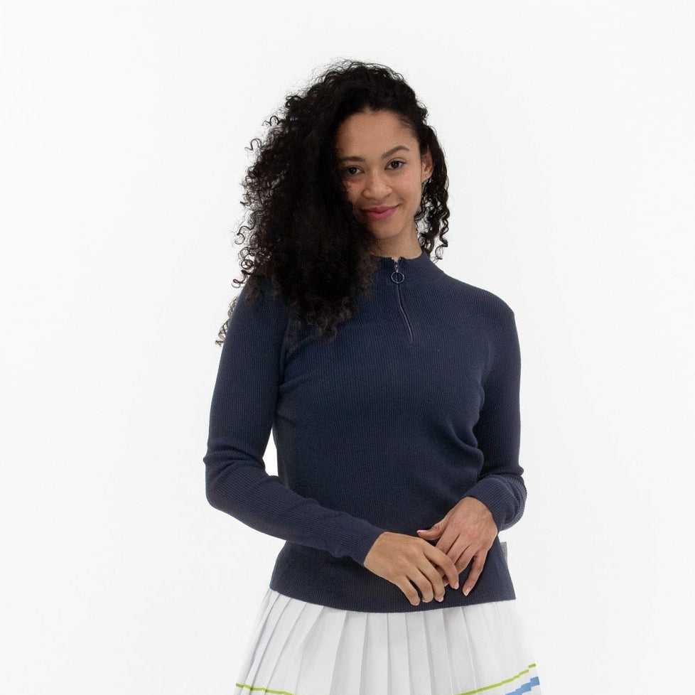 Woman wearing a navy long-sleeve top and white skirt with blue accents on a white background